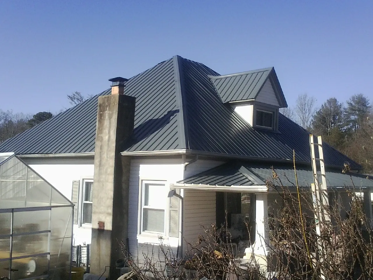 Dark blue standing seam metal roof on a white farmhouse with dormer — Slate & Tile Roof Repair by Roofing Brothers in Maple Falls