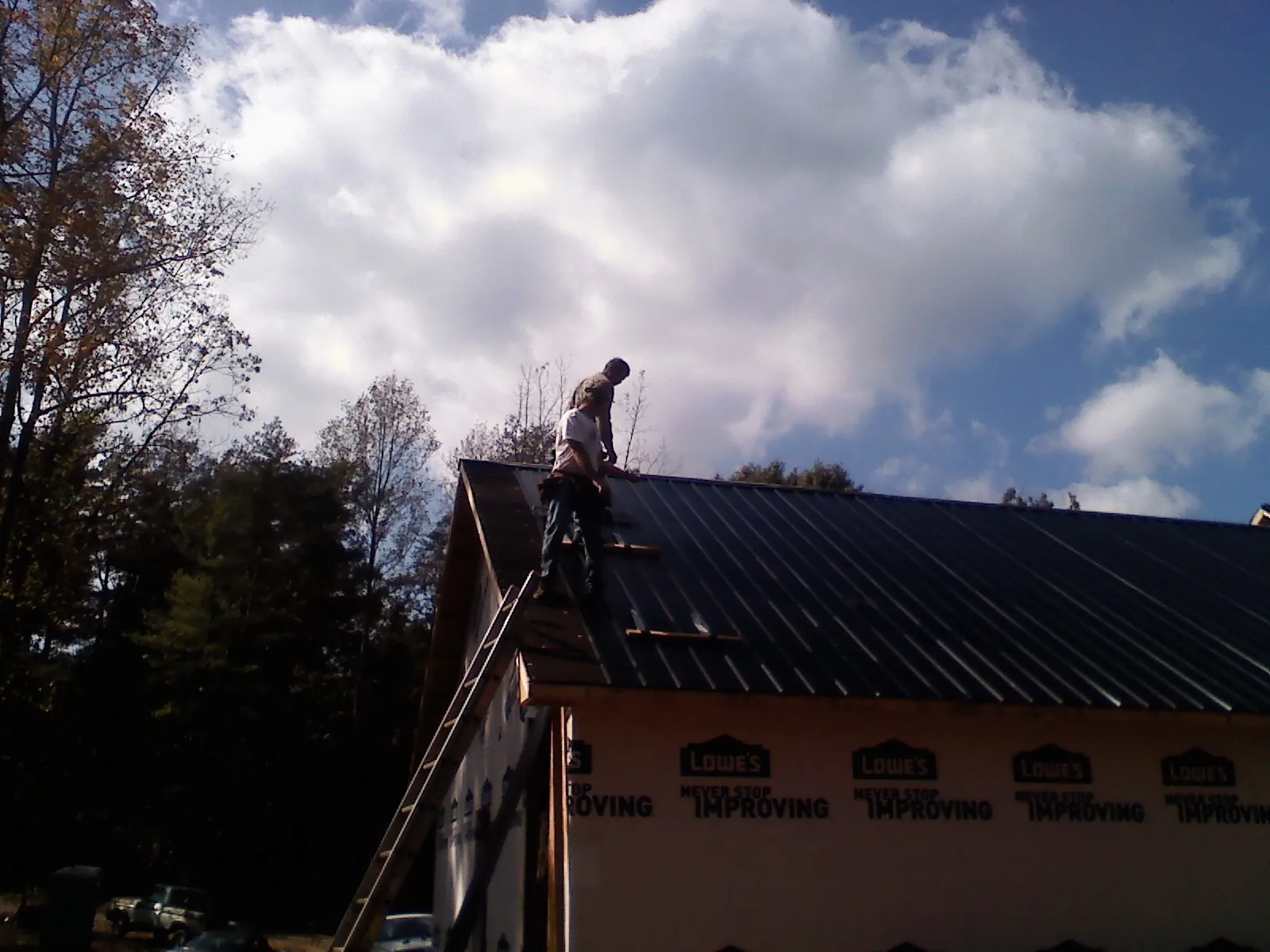 Roofer fastening dark metal panels high against a cloudy sky, from a Roof Inspection job in Maple Falls