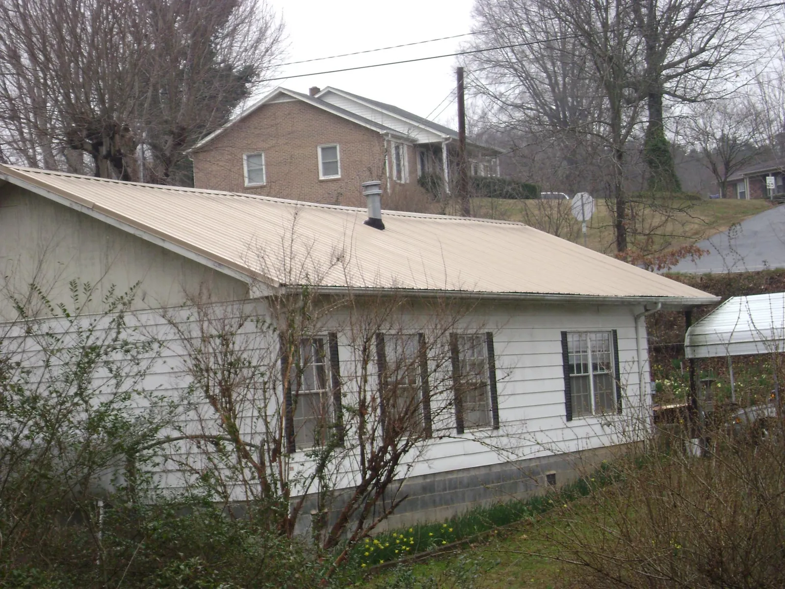 Tan metal roof on a white sided house set into a hillside — Commercial Roofing by Roofing Brothers in Maple Falls